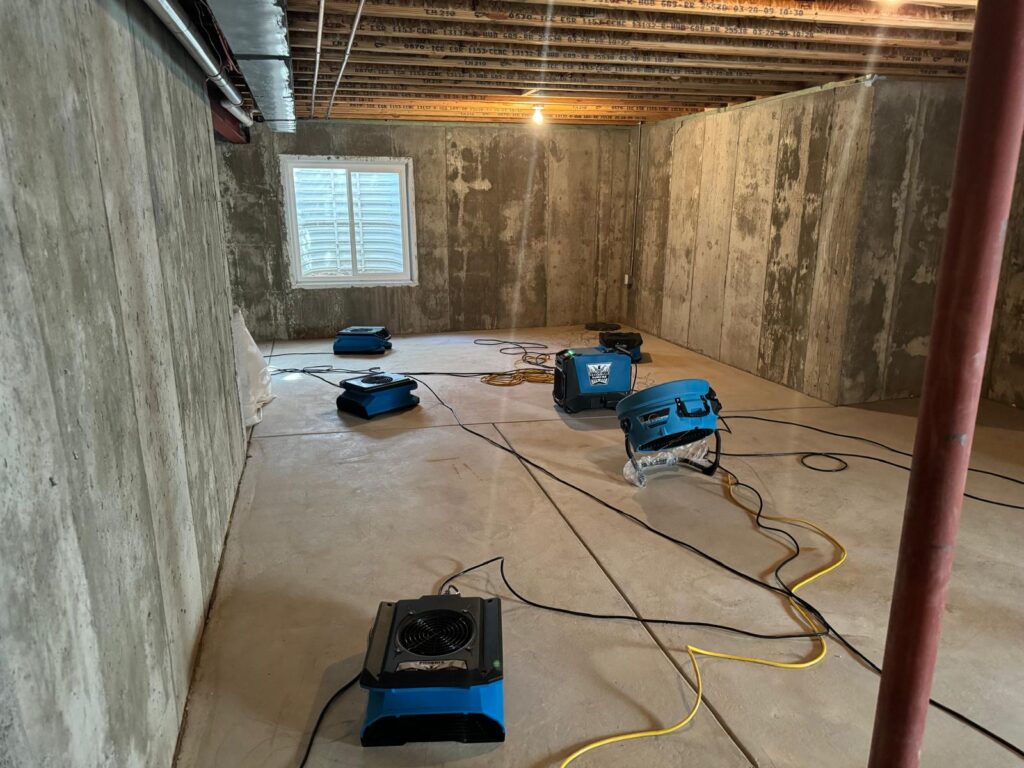 Professional water damage restoration equipment in a flooded basement, featuring industrial fans and dehumidifiers for effective moisture removal and drying process.