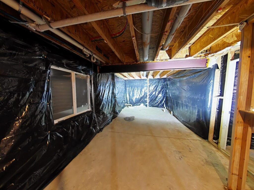 Interior space with black plastic sheeting covering walls, indicating mold remediation process, exposed beams and concrete floor, emphasizing professional containment measures for mold removal.